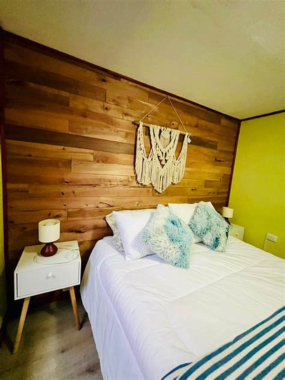Dormitorio con revestimiento de madera, cama hecha y un macramé colgado en la pared.