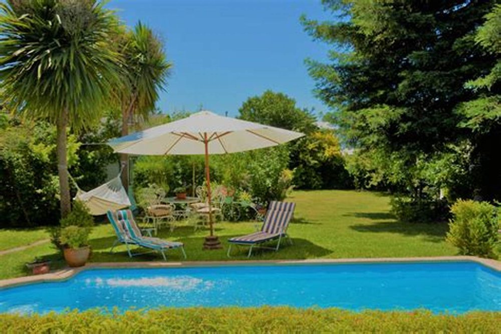 El jardín con la piscina y las tumbonas bajo el quitasol.