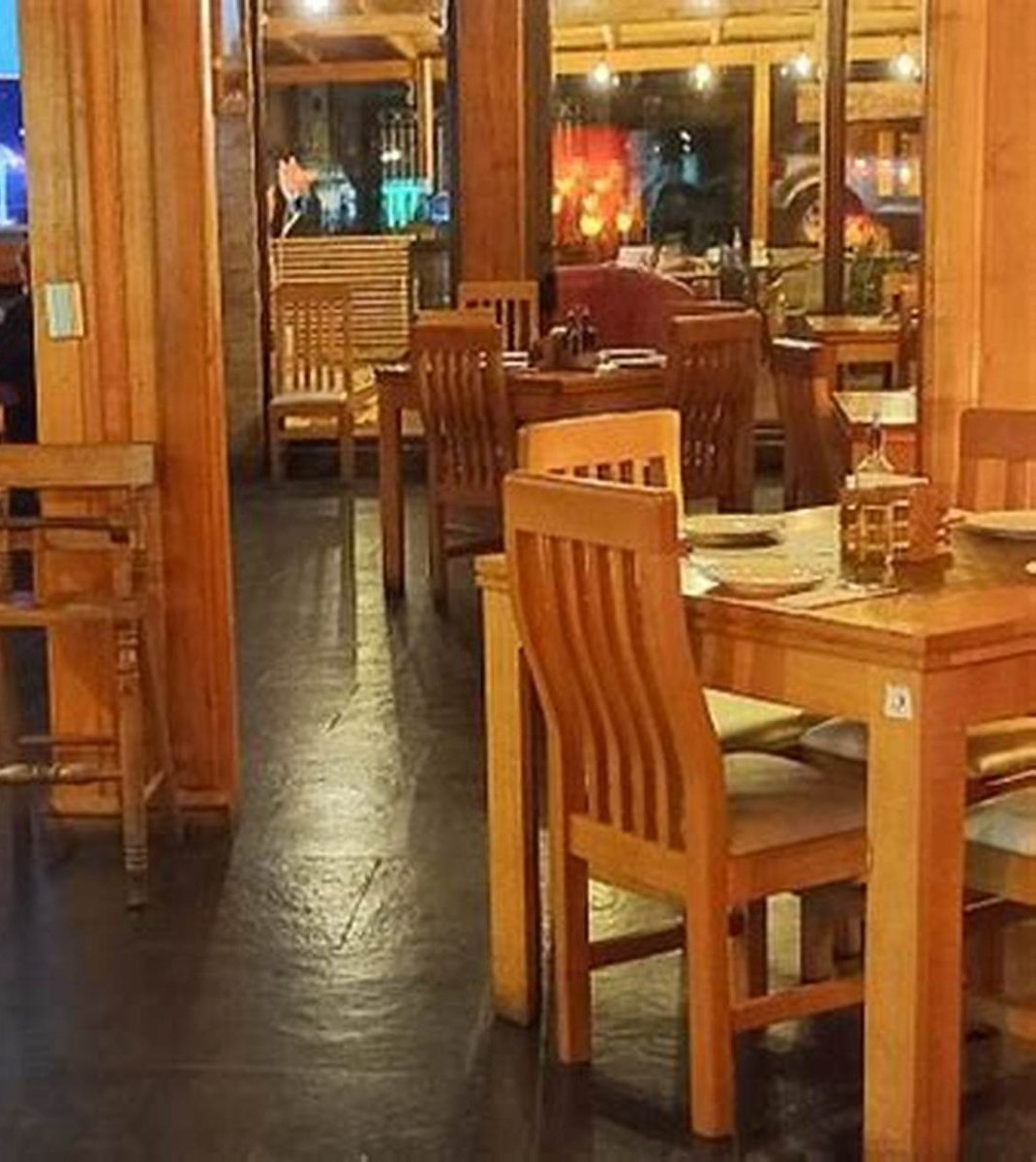 El salón con mesas y sillas de madera puestas, iluminado de noche.
