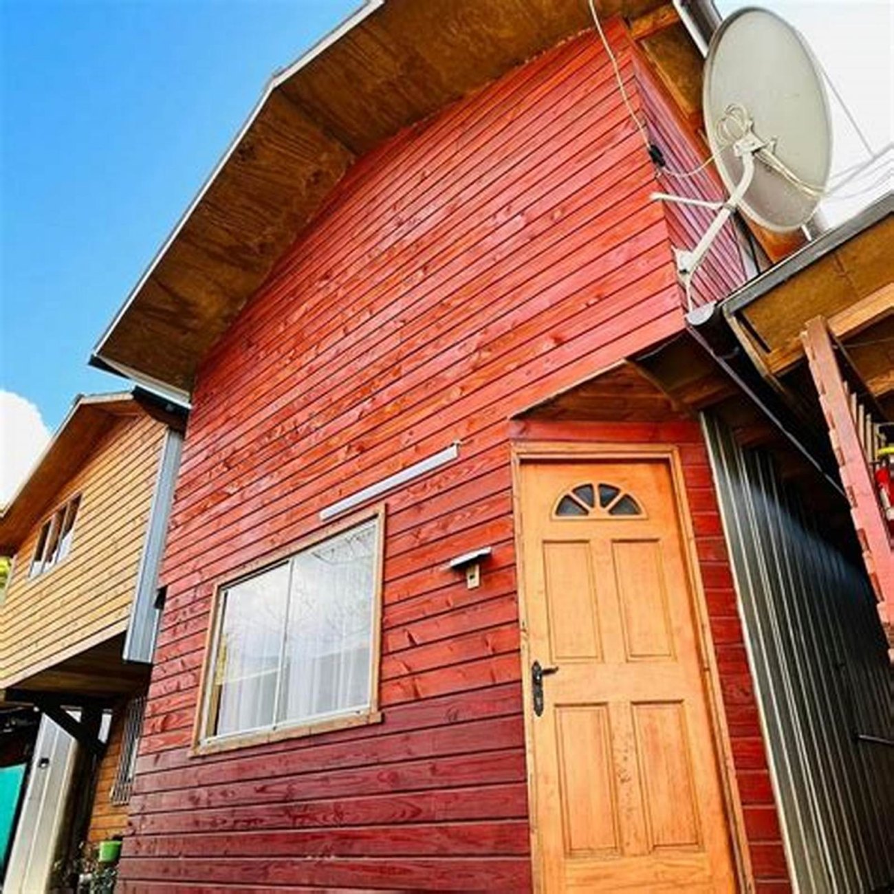 La cabaña roja con su puerta de madera y la antena en el techo.