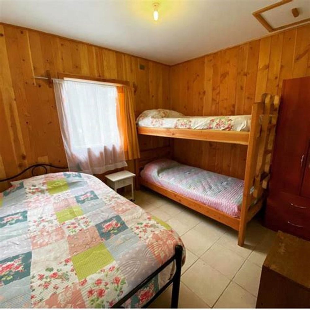 Dormitorio con camarote y cama de plaza y media, paredes de madera y ventana con cortina.