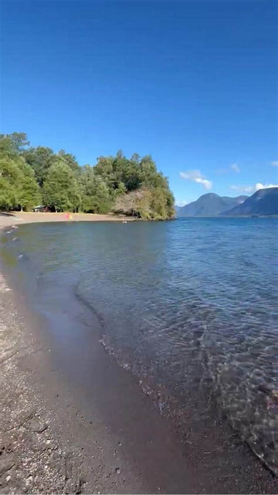 La orilla del lago con el agua clara y los cerros al fondo.