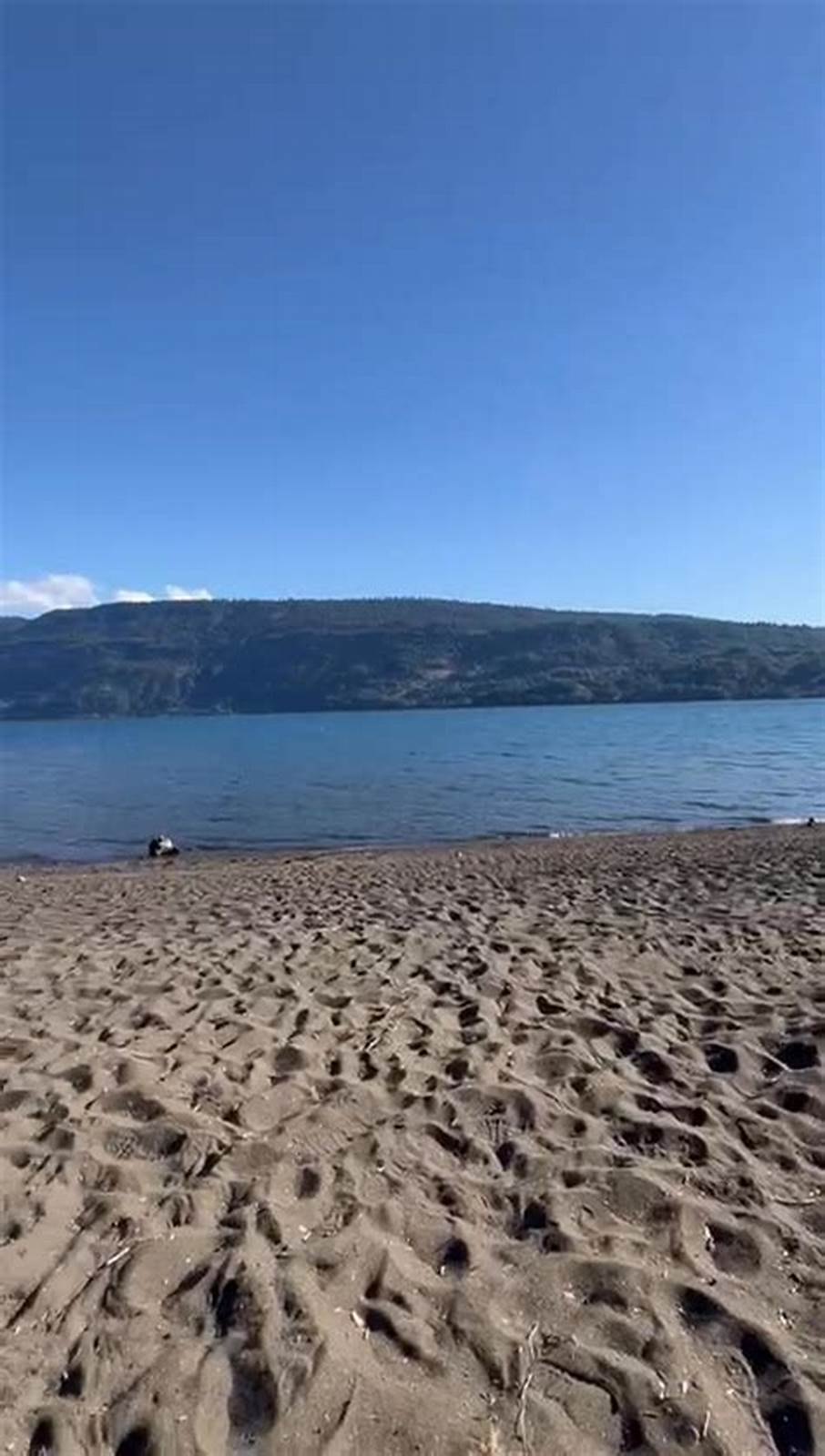La playa de arena con el lago y la cadena de cerros al frente.