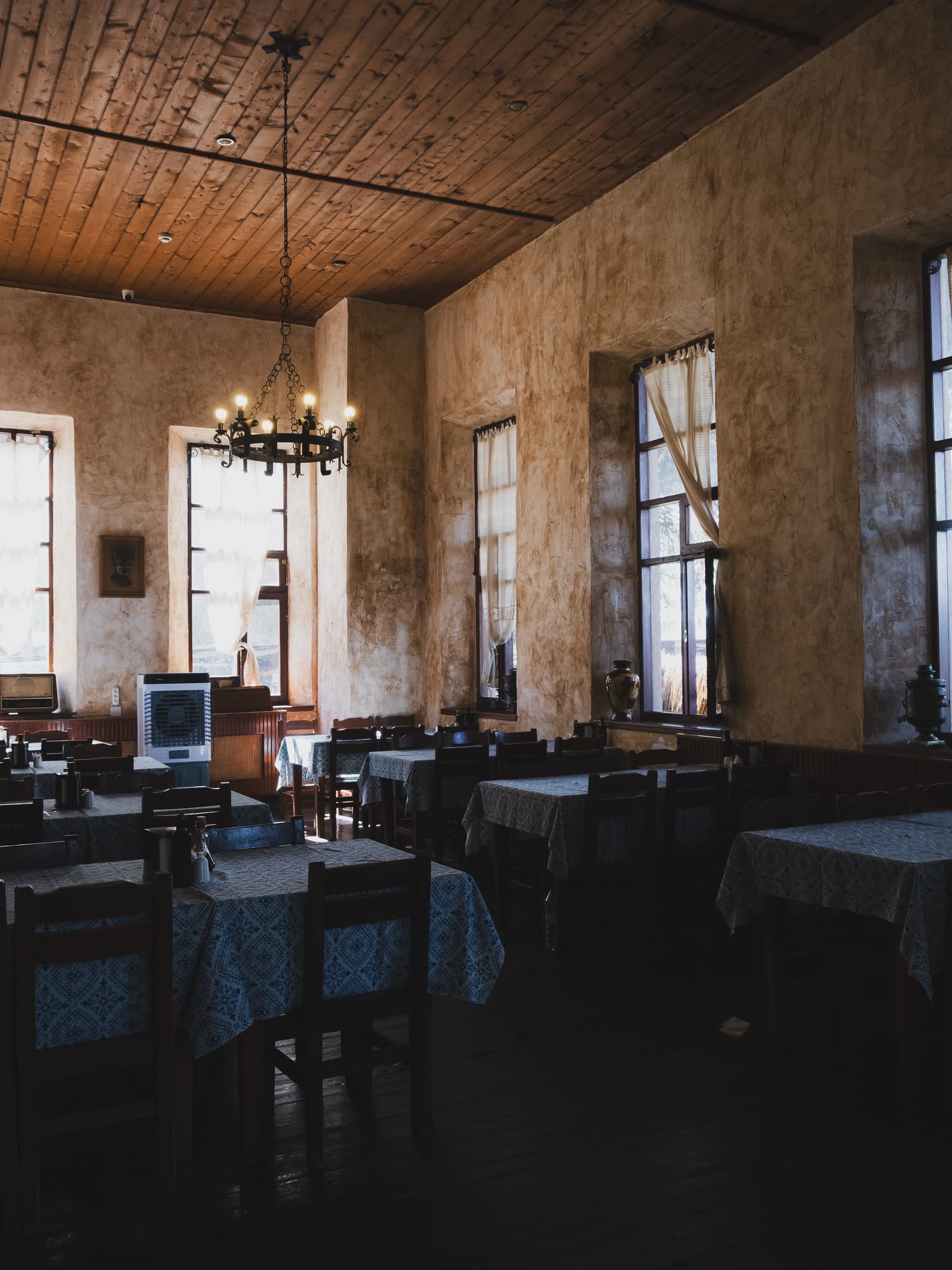 Comedor antiguo de techo de tablas, mesas con mantel y ventanas altas, sin gente