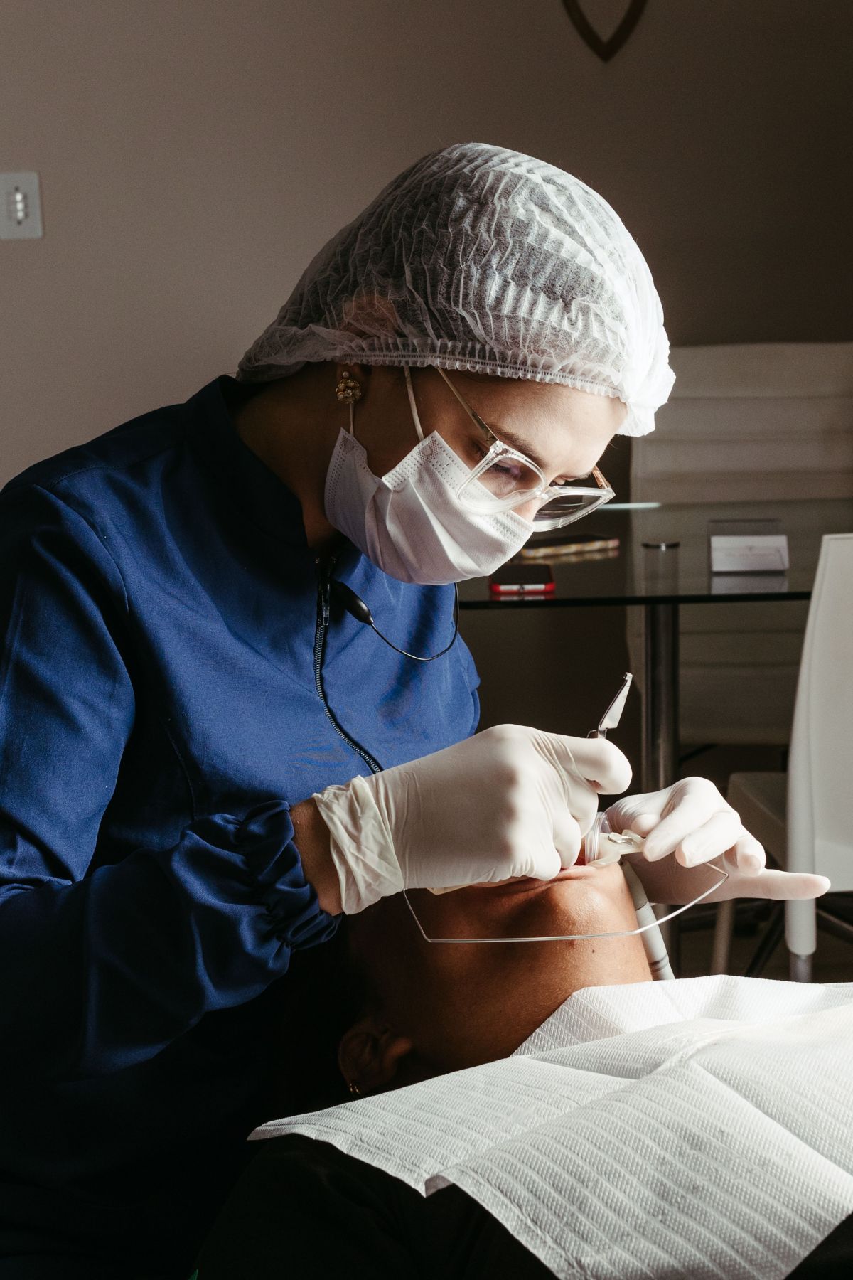 Odontóloga con gorro y mascarilla trabajando sobre un paciente recostado