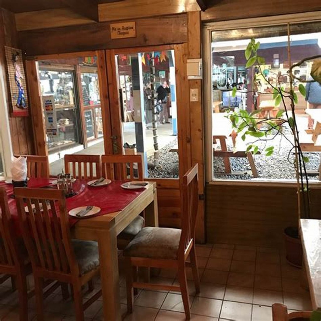 El salón por dentro, con las mesas de mantel rojo y los ventanales al jardín.