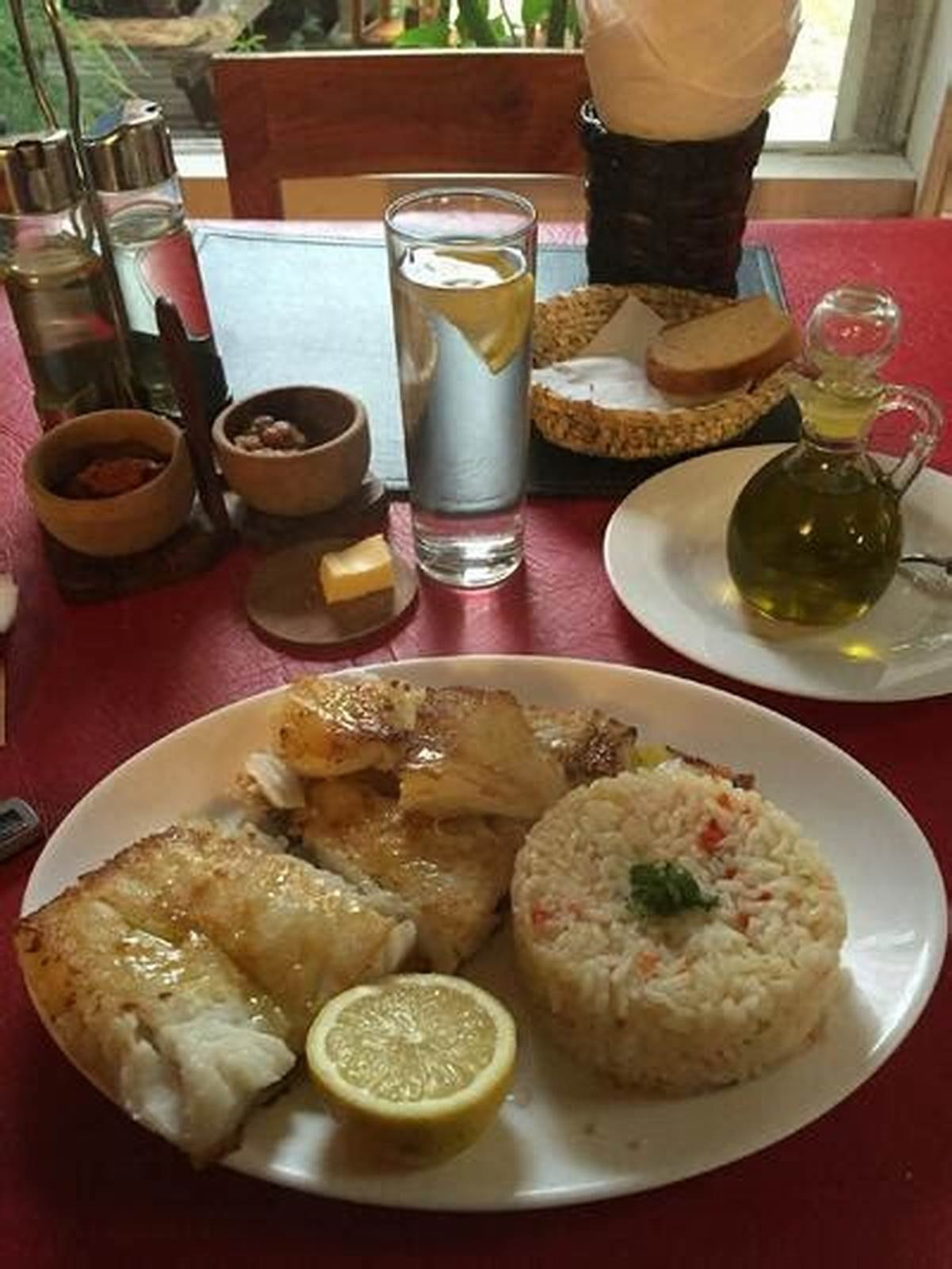 Un plato de pescado con arroz, servido en la mesa con el aceite y el pan al lado.