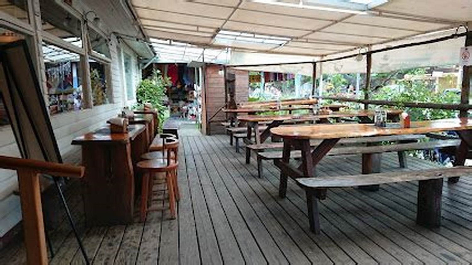 La terraza cubierta, con las mesas largas de madera puestas y el suelo de tablas.