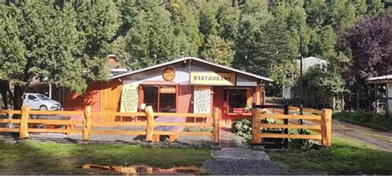 La fachada de madera del restaurante entre los árboles, con el letrero y la reja de troncos.