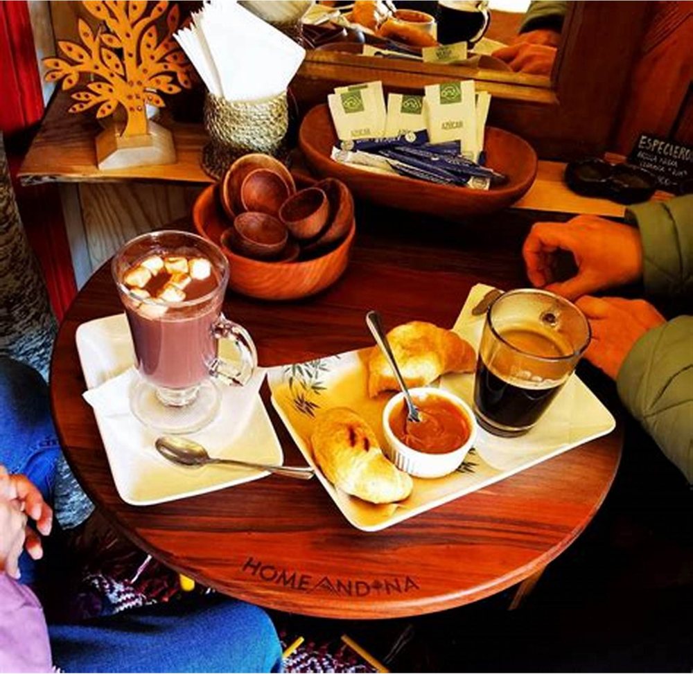 Chocolate caliente, café y sopaipillas servidos en la mesa de madera.