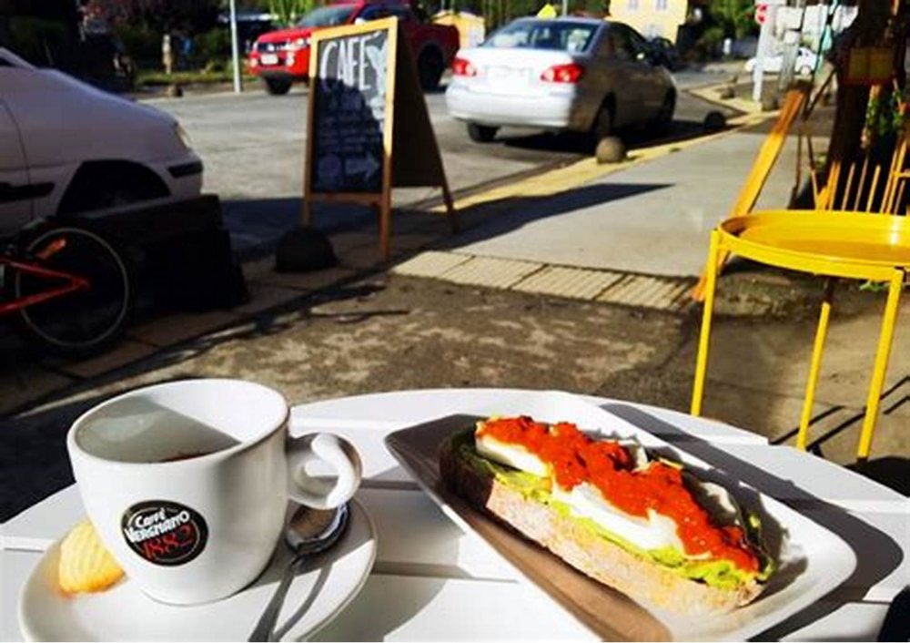 Un café con un sándwich abierto, en la mesa de la vereda.