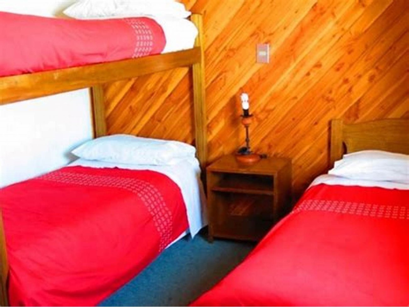 Dormitorio con paredes de madera, dos camas y una mesa de noche.