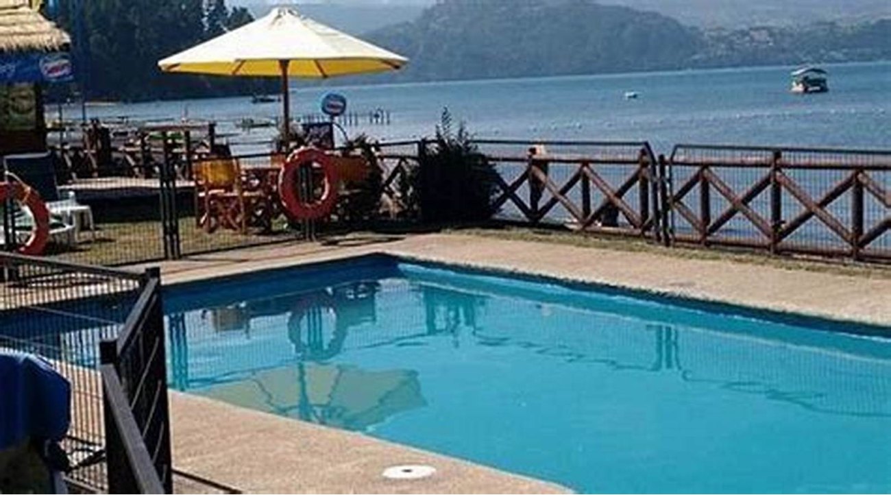 La piscina con el quitasol y, detrás, el lago y los cerros.