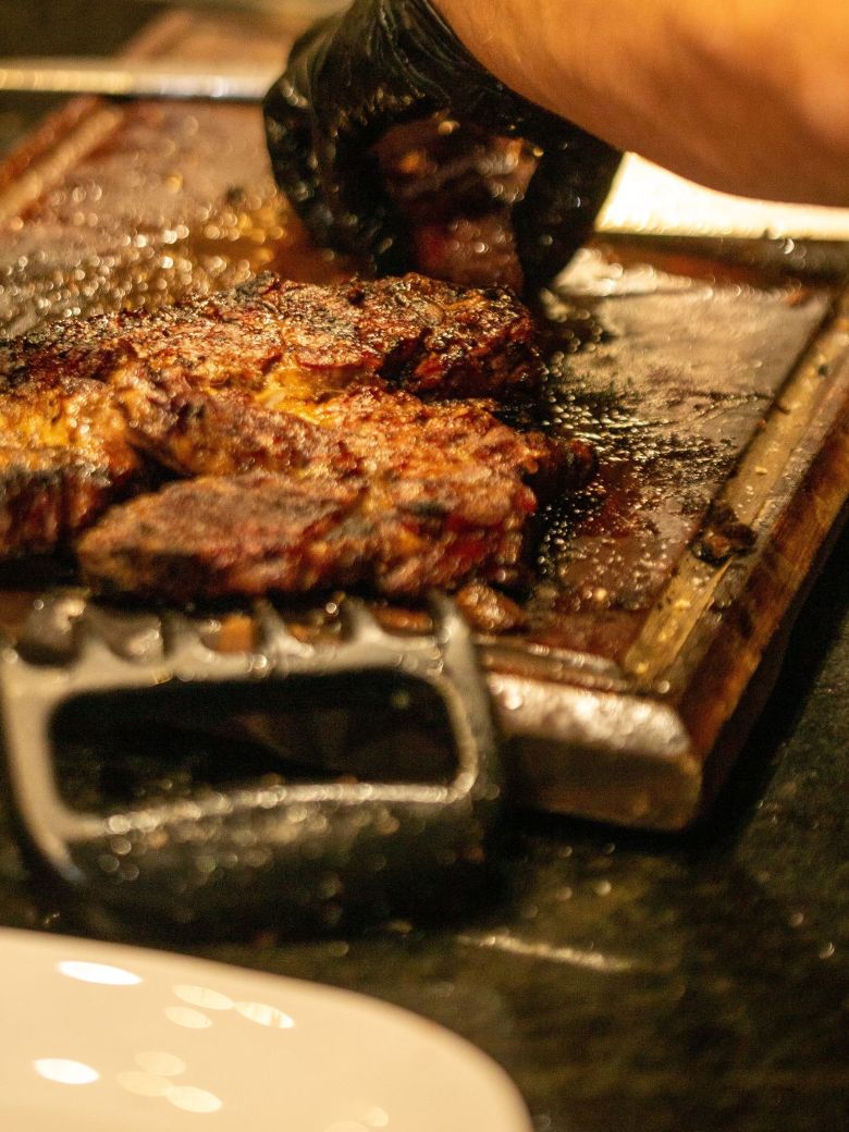 Cortes de carne sazonándose sobre una tabla de madera junto a la plancha.