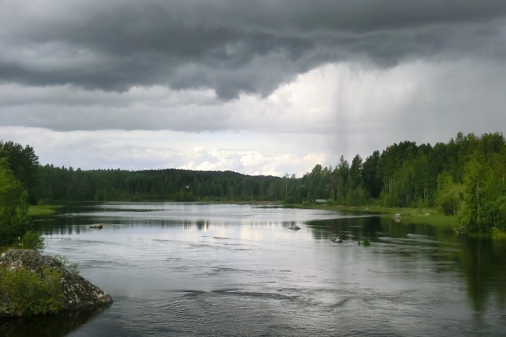 Nubarrones de lluvia sobre el lago y el bosque de la orilla.
