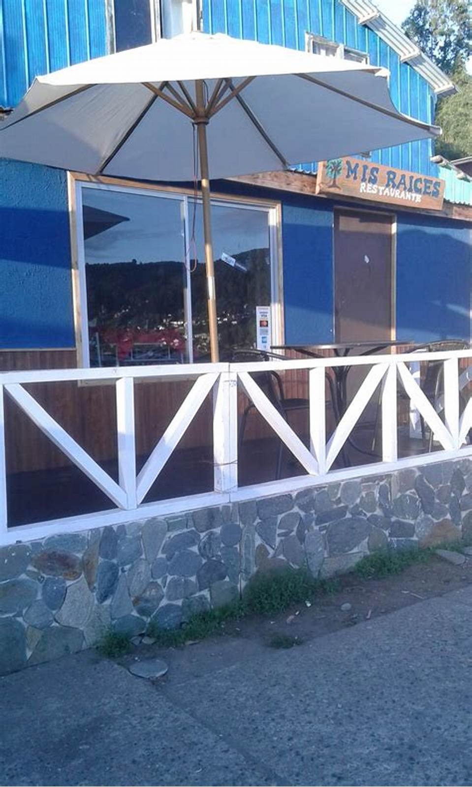La terraza del local con su quitasol, junto a la baranda blanca que da a la calle.