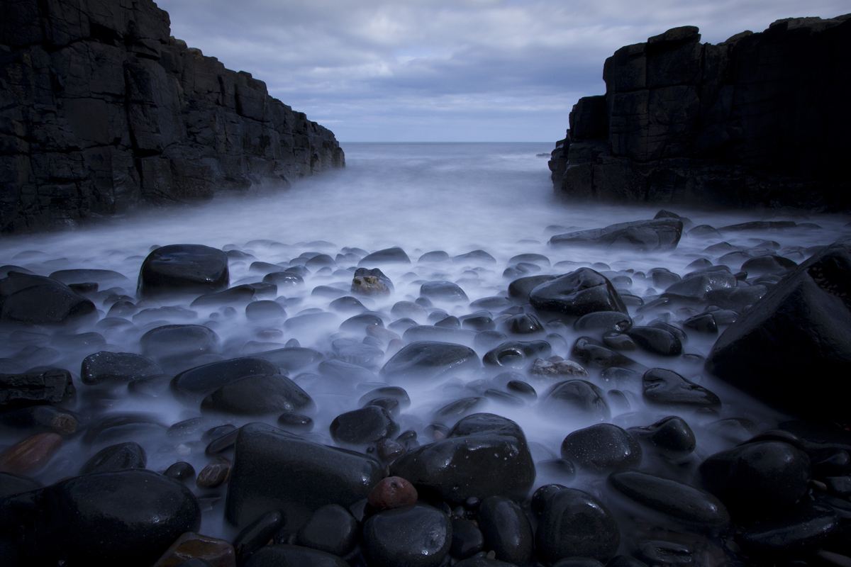 Piedras redondas de la orilla en marea baja, entre dos paredes de roca.