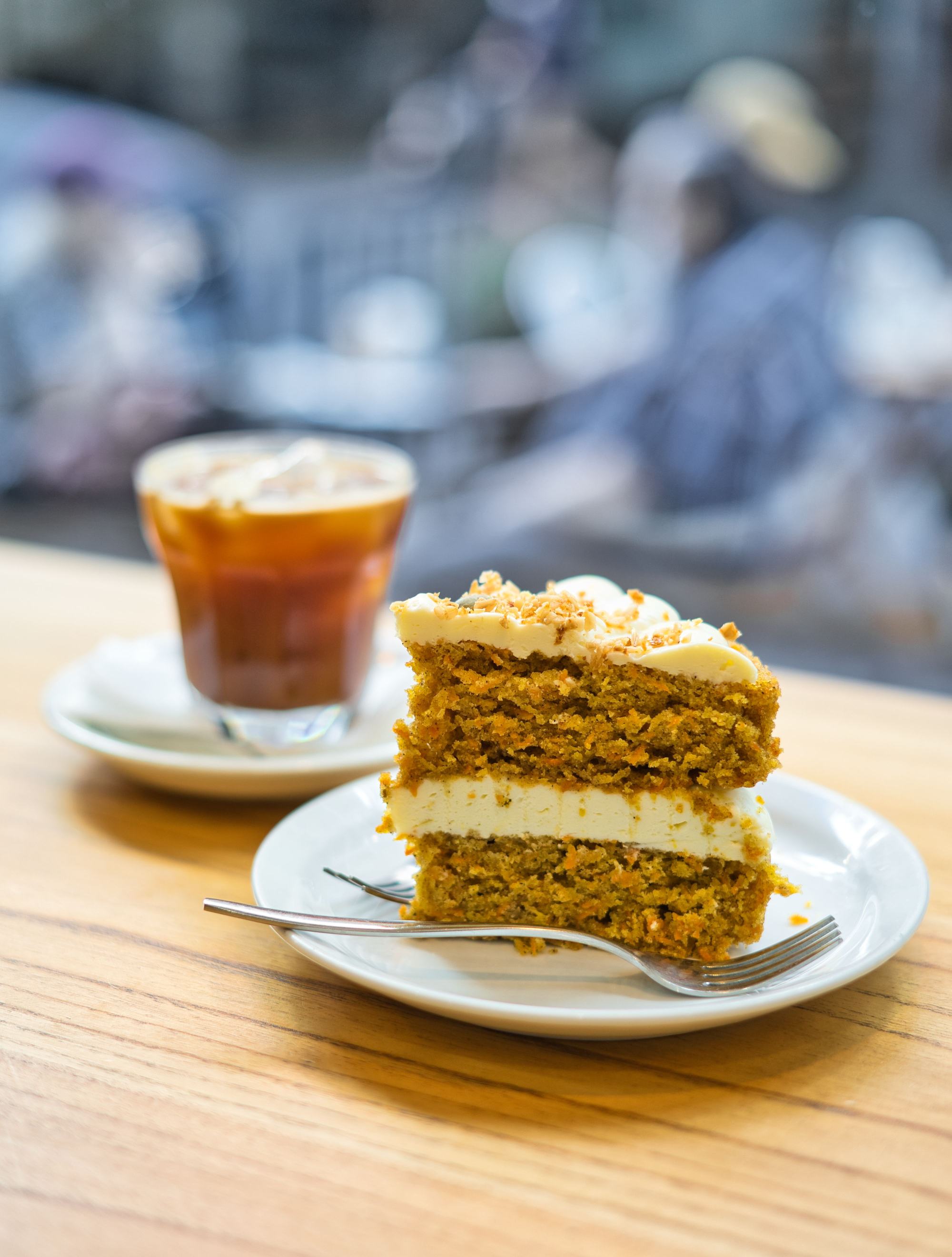Trozo de torta en un plato con un café al lado, sobre una mesa de madera